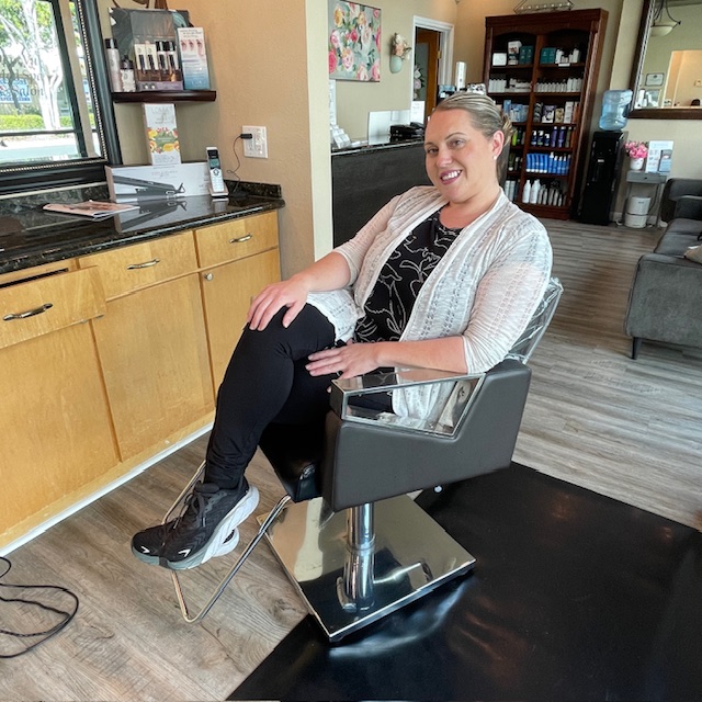 Julianne sitting in a salon chair smiling at the camera.