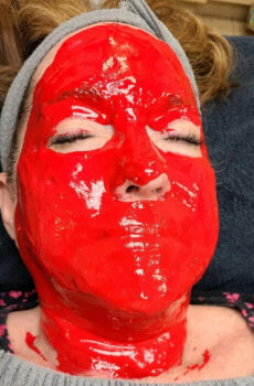 Woman on table with red peel mask on.